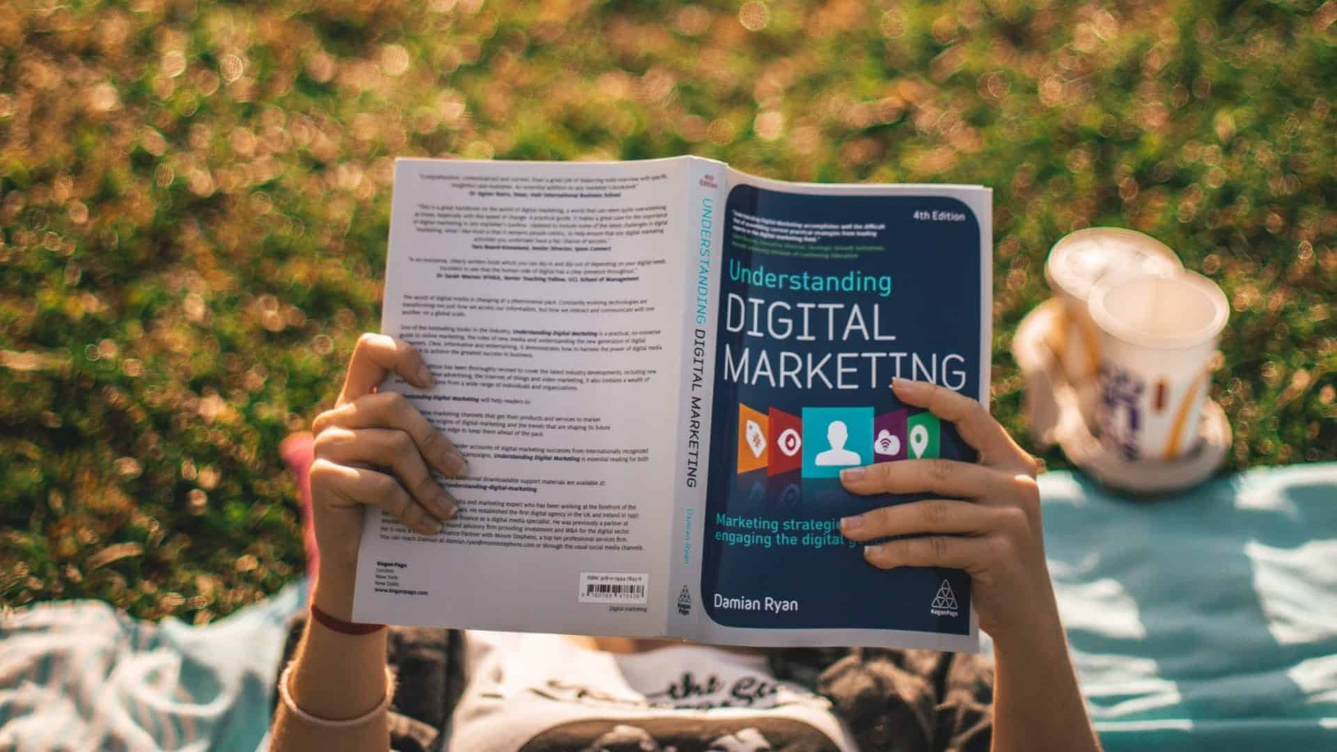 Person reading "Understanding Digital Marketing" book on a grass lawn