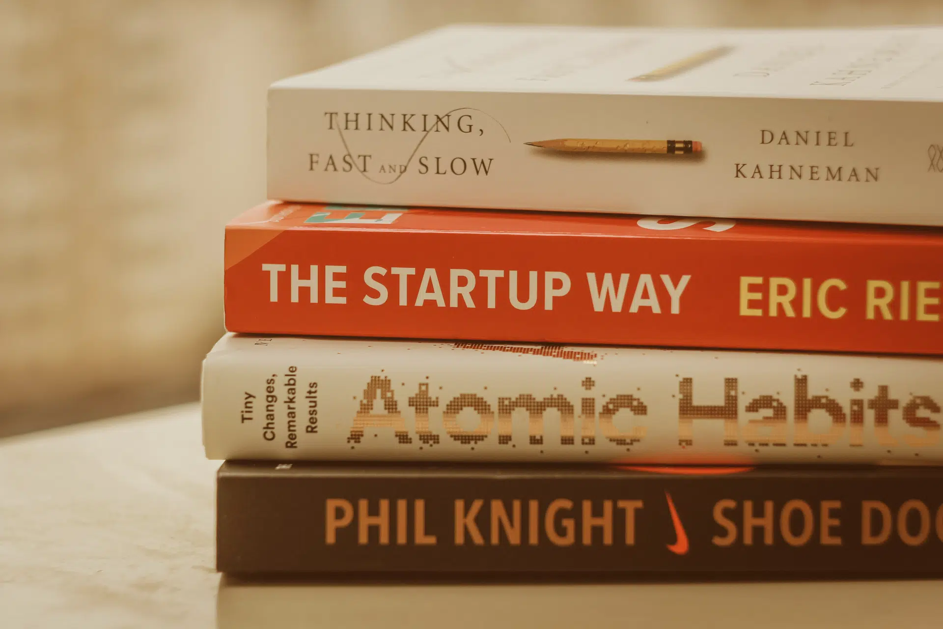 Stack of books including "Atomic Habits", "Thinking, Fast and Slow" with an orange tinge